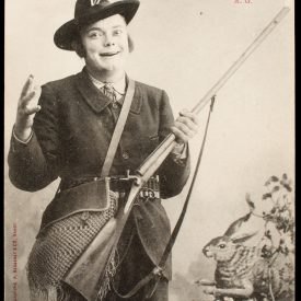 Comic French postcard showing a grinning male hunter with a side-by-side pinfire shotgun, game bag, cartridge belt, and rabbit prop.